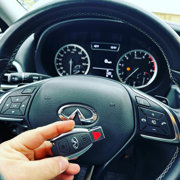 A new key fob for an Infinity vehicle is held in front of the steering wheel.